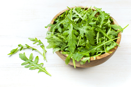 Fresh green arugula leaves on wooden bowl, rucola salad on white wooden rustic background with place for text. Selective focus. Rocket salad or arugula, healthy food, diet. Nutrition conceptの写真素材