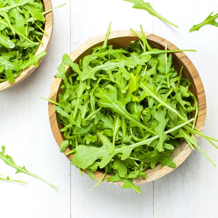 Fresh green arugula leaves on wooden bowl, rucola salad on white wooden rustic background top view with place for text. Rocket salad or arugula, healthy food, diet. Nutrition conceptの写真素材