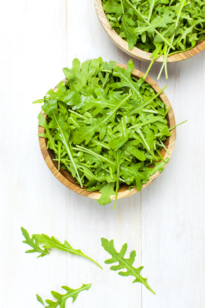 Fresh green arugula leaves on wooden bowl, rucola salad on white wooden rustic background top view with place for text. Rocket salad or arugula, healthy food, diet. Nutrition conceptの写真素材
