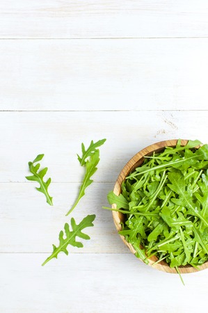 Fresh green arugula leaves on wooden bowl, rucola salad on white wooden rustic background top view with place for text. Rocket salad or arugula, healthy food, diet. Nutrition conceptの写真素材