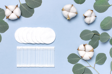 Cotton Cosmetic Makeup Removers Tampons. Spa concept. Flat lay background with cotton flowers, cotton pads, eared sticks, fresh eucalyptus twigs. Hygienic sanitary swabs on blue background Top view.の写真素材