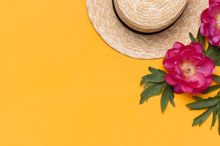 Women's straw hat and beautiful pink flowers peonies on bright yellow background. Summer holiday background. Flat lay, top view, copy space. Travel Vacation Concept, shopping. Trendy feminine fashion.の写真素材