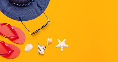 Summer beach sea accessories. Coral flip flops, blue straw hat, sunglasses, shells, starfish on yellow background top view flat lay copy space. Summer background. Holiday vacation travel conceptの写真素材