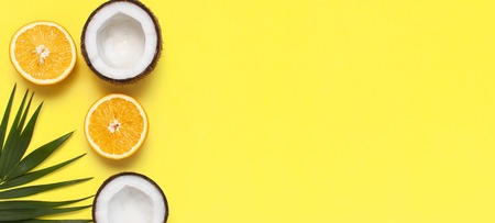 Summer tropical composition. Green tropical leaves of palm trees and monstera, coconut, orange on bright yellow background. Flat lay, top view, copy space. Creative background food, fruit.の写真素材