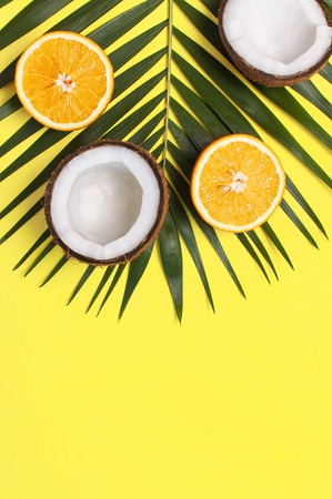 Summer tropical composition. Green tropical leaves of palm trees and monstera, coconut, orange on bright yellow background. Flat lay, top view, copy space. Creative background food, fruit.の写真素材