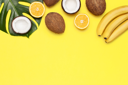 Summer tropical composition. Green tropical leaves of palm trees and monstera, coconut, orange, bananas on bright yellow background. Flat lay, top view, copy space. Creative background food, fruit.の写真素材