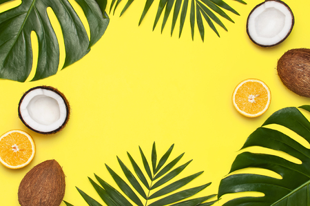 Summer tropical composition. Frame of Green tropical leaves of palm trees and monstera, coconut, orange on bright yellow background. Flat lay, top view, copy space. Creative background food, fruit.の写真素材
