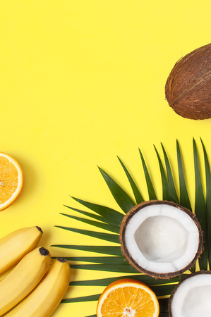 Summer tropical composition. Green tropical leaves of palm trees and monstera, coconut, orange, bananas on bright yellow background. Flat lay, top view, copy space. Creative background food, fruit.の写真素材