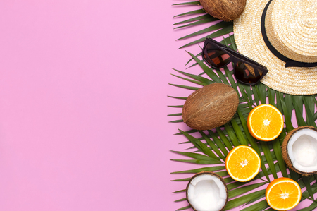 Summer fashion flat lay. Round trendy rattan bag straw hat sunglasses tropical palm leaves coconut orange on pink background. Top view copy space Trendy bamboo bag Creative background vacation concept.の写真素材