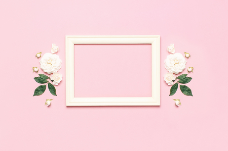 Flowers composition. Wooden white photo frame, white fresh roses and green leaves on gentle pink background. Flat lay, top view, copy space. Flower card, greeting, holiday mockup. Valentine's Day.の写真素材