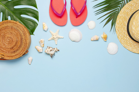 Summer composition flat lay. Round trendy rattan bag straw hat coral flip flops tropical palm leaves coconut sunscreen seashells on blue background. Top view copy space. Creative fashion backdrop.の写真素材