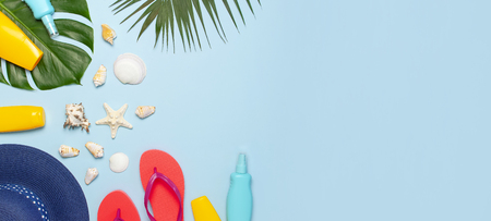 Summer fashion flat lay. Blue hat coral flip flops tropical palm leaves sunscreen seashells on blue background. Top view copy space. Creative fashion vacation background.の写真素材
