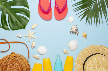 Summer composition flat lay. Round trendy rattan bag straw hat coral flip flops tropical palm leaves coconut sunscreen seashells on blue background. Top view copy space. Creative fashion backdrop.の写真素材