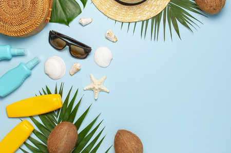 Summer composition flat lay. Round trendy rattan bag straw hat sunglasses tropical palm leaves coconut sunscreen seashells on blue background. Top view copy space. Creative fashion vacation backdrop.の写真素材