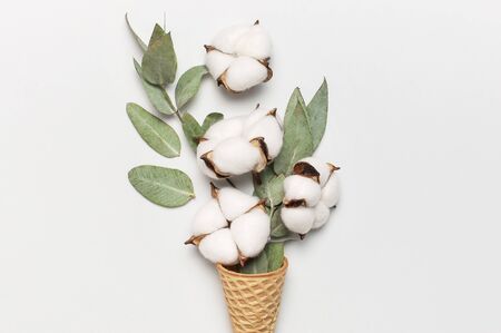 Waffle cone with bouquet of cotton flowers and fresh eucalyptus twigs on light gray background. Creative Delicate white cotton flowers minimal concept. Flat lay top view copy spaceの写真素材