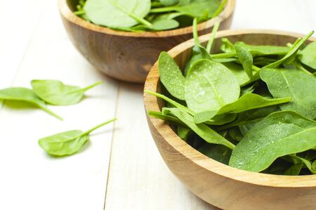 Fresh green spinach leaves on wooden bowl on white wooden rustic background top view copy space. Baby young spinach leaves, Ingredient for salad, healthy food, diet. Nutrition conceptの写真素材