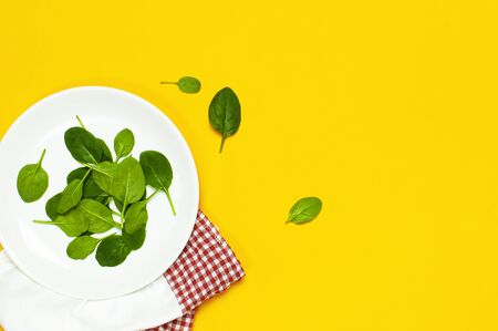 Fresh green spinach leaves on a white plate kitchen towel on bright yellow background flat lay top view copy space. Baby young spinach leaves, healthy food, diet. Creative food conceptの写真素材