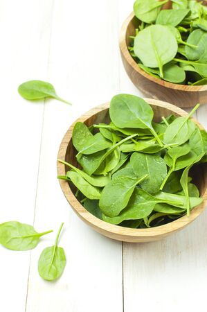 Fresh green spinach leaves on wooden bowl on white wooden rustic background top view copy space. Baby young spinach leaves, Ingredient for salad, healthy food, diet. Nutrition conceptの写真素材