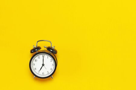 Black retro alarm clock on yellow background top view Flat lay copy space. Minimalistic background, concept of time, deadline, time to work, morning.の写真素材