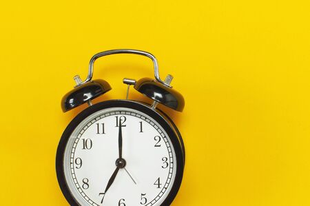 Black retro alarm clock on yellow background top view Flat lay copy space. Minimalistic background, concept of time, deadline, time to work, morning.の写真素材