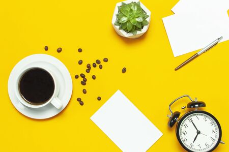 Flat lay cup black coffee, coffee beans, black alarm clock, pens, white cards, succulent on yellow background top view copy space. Creative Concept time to work, female desktop, coffee background.の写真素材