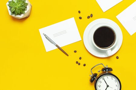 Flat lay cup black coffee, coffee beans, black alarm clock, pens, white cards, succulent on yellow background top view copy space. Creative Concept time to work, female desktop, coffee background.の写真素材