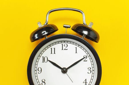 Black retro alarm clock on yellow background top view Flat lay copy space. Minimalistic background, concept of time, deadline, time to work, morning.の写真素材