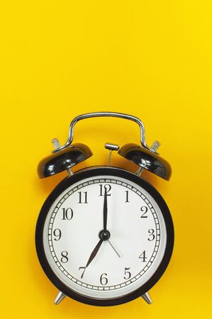 Black retro alarm clock on yellow background top view Flat lay copy space. Minimalistic background, concept of time, deadline, time to work, morning.の写真素材