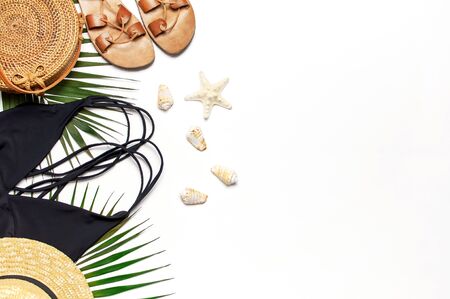 Woman's beach accessories flat lay. Round trendy rattan bag straw hat black swimsuit leather sandals tropical palm leaves seashells on white background. Top view copy space. Summer backdrop.の写真素材