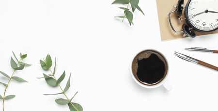 Flat lay cup of black coffee, black alarm clock, notebook, diary, eucalyptus on white background top view copy space. Minimalistic food concept, Feminine desk workspace, time to work coffee background.の写真素材