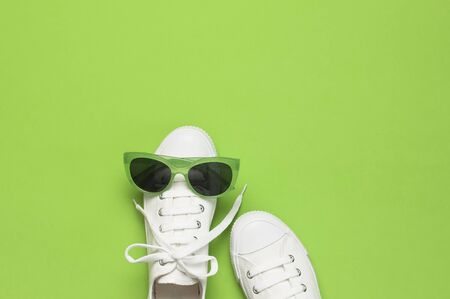 White female fashion sneakers and trendy sunglasses on green background. Flat lay top view copy space. Women's shoes, accessories. Stylish white sneakers. Creative concept Fashion blog or magazine.の写真素材