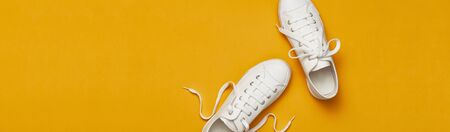 White female fashion sneakers on yellow orange background. Flat lay top view copy space. Women's shoes. Stylish white sneakers. Fashion blog or magazine concept. Minimalistic shoe background, sport.の写真素材
