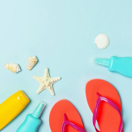 Summer beach sea accessories. Coral flip flops, shells, starfish, yellow sunscreen bottle, body spray on blue background top view flat lay copy space. Summer background Holiday vacation travel concept.の写真素材