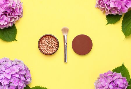 Set of decorative cosmetics makeup brushes, blush face balls, pink hydrangea flowers on yellow background top view Flat lay copy space. Beauty blogger concept. Fashion background. Makeup accessories.の写真素材
