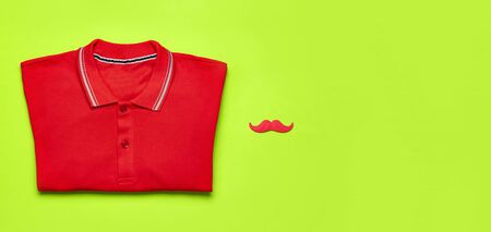 Creative party decoration concept. Red mustache, red polo shirt, props for photo booths, carnival parties on green background top view flat lay copy space. Father's day, Men's clothes accessories.の写真素材