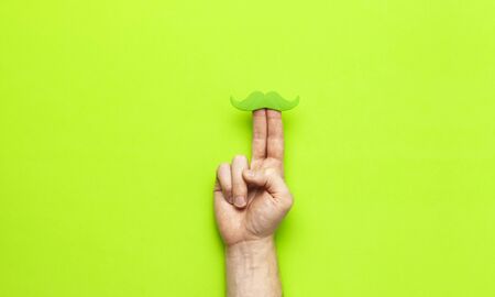 Creative party decoration concept Men's hands hold green mustache, props for photo booths, carnival parties on green background top view flat lay copy space Father's day Men's health awareness month.の写真素材