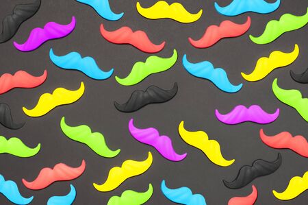 Creative party decoration concept. Pattern of colorful bright mustache, props for photo booths, carnival parties on black background top view flat lay copy space. Father's day, Men's health awareness month.の写真素材