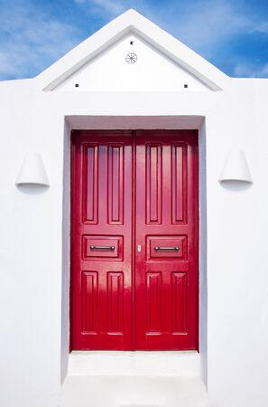 Beautiful old red door on white facade of greek architecture against the blue sky, Santorini island, Greece, Europe. Beautiful details of the island of Santorini. Famous travel destination.の写真素材