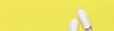White female fashion sneakers on yellow background. Flat lay top view copy space. Women's shoes. Stylish white sneakers. Fashion blog or magazine concept. Minimalistic shoe background long banner.の写真素材