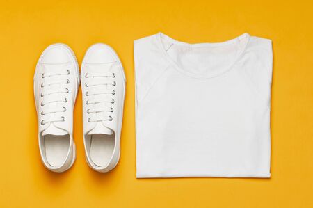 White female fashion sneakers, white T-shirt on yellow orange background. Flat lay top view copy space. Women's shoes. Stylish white sneakers. Fashion blog or magazine concept. Shoe background sportの写真素材