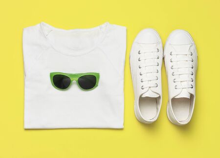 White female fashion sneakers, trendy sunglasses, white T-shirt on yellow background. Flat lay top view copy space. Women's shoes, accessories. Stylish white sneakers. Creative concept Fashion blog.の写真素材
