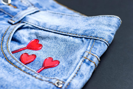 Blue jeans and red hearts from pocket on black background top view flat lay. Detail of nice blue...