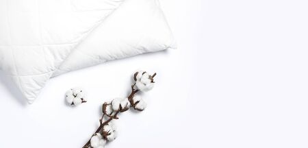 Soft white quilted pillow and branch of cotton on light background top view. Clean pillow, interior item, bedding mockup design template.の写真素材