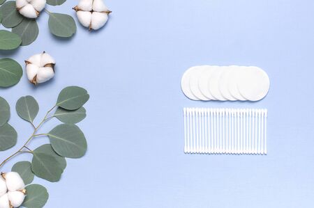 Cotton Cosmetic Makeup Removers Tampons. Spa concept. Flat lay background with cotton flowers, cotton pads, eared sticks, fresh eucalyptus twigs. Hygienic sanitary swabs on blue background Top view.の写真素材