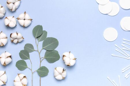 Cotton Cosmetic Makeup Removers Tampons. Spa concept. Flat lay background with cotton flowers, cotton pads, eared sticks, fresh eucalyptus twigs. Hygienic sanitary swabs on blue background Top view.の写真素材