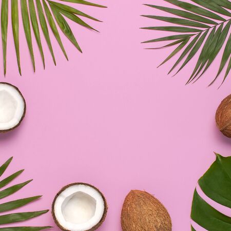 Frame of tropical leaves and fresh coconut on pink background. Flat lay, top view, copy space. Summer background, nature. Healthy cooking. Creative healthy food concept, half of coconut.の写真素材