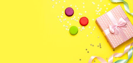 Gift or present box, beautiful festive ribbon, cake macaron or macaroon, confetti on yellow background top view. Flat lay composition for celebration, birthday, Valentines Day, March 8, mother day.の写真素材