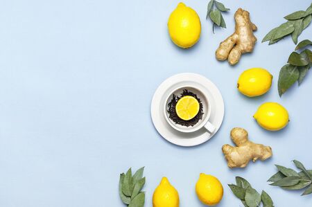 Creative food concept. Fresh ginger root, cup tea with brewing inside, lemon, eucalyptus leaves on blue background. Flat lay top view copy space. Minimalistic style seasoning spice ingredient for tea.の写真素材