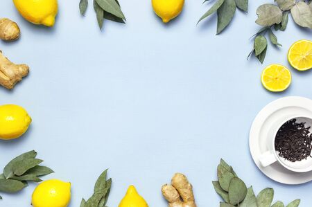 Creative food concept. Fresh ginger root, cup tea with brewing inside, lemon, eucalyptus leaves on blue background. Flat lay top view copy space. Minimalistic style seasoning spice ingredient for tea.の写真素材