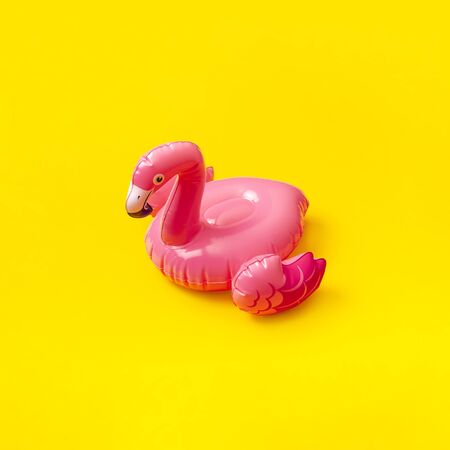 Creative summer beach concept. Inflatable pink mini flamingo on yellow background, pool float party. Flat lay, copy space. Flamingo Trend Inflatable Toy. Summer background. Layout for design.の写真素材